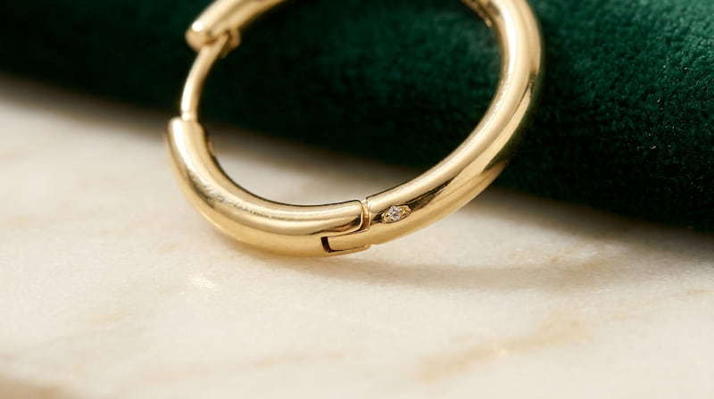 Technical detail of a hinge closure in gold hoop earrings showing how the pin retracts into the tube.